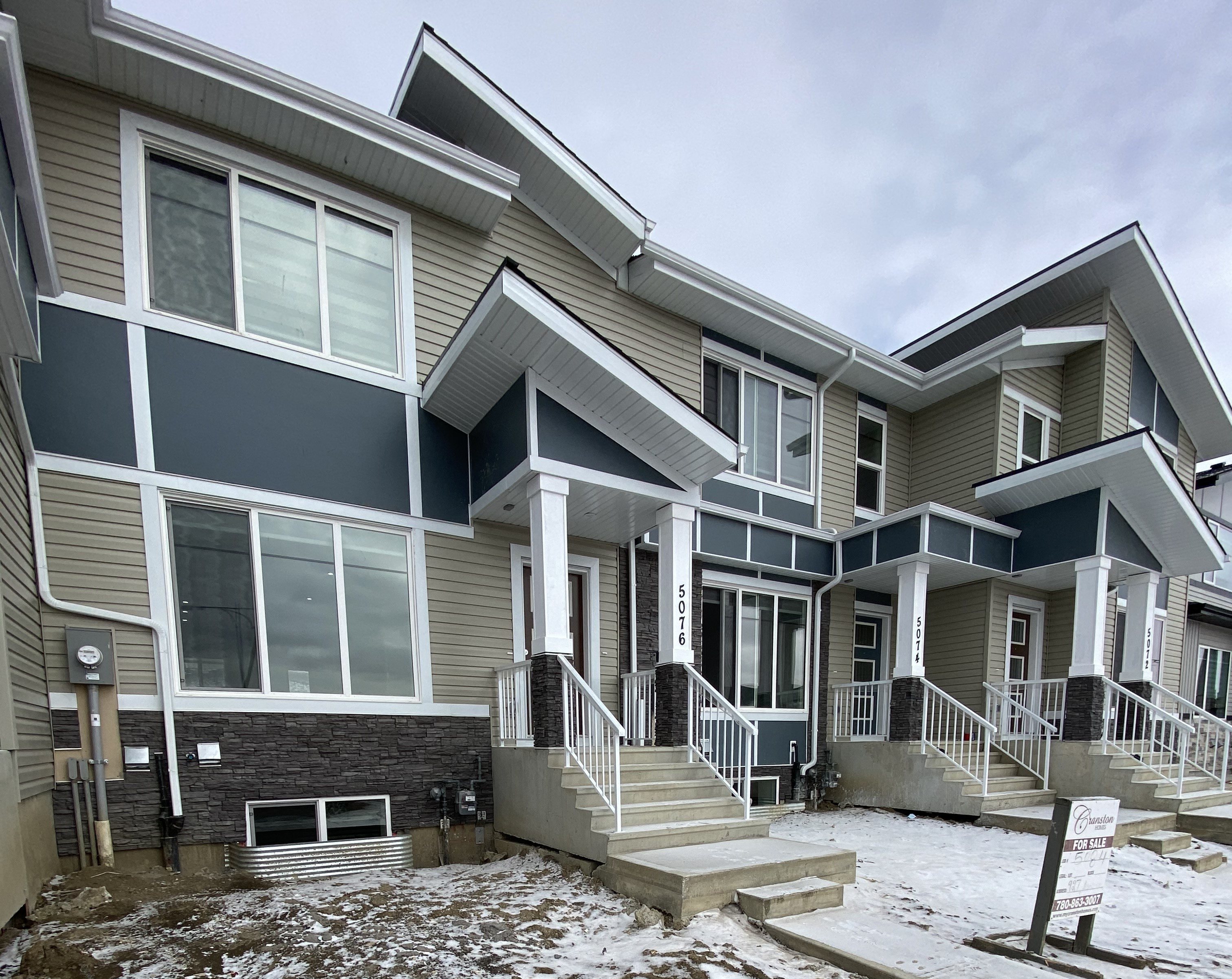 A house with a grey and white exterior and a snowy ground.